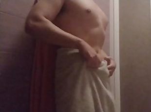 Un joven hombre musculoso se seca con la toalla después de la ducha y se echa crema por su cuerpo
